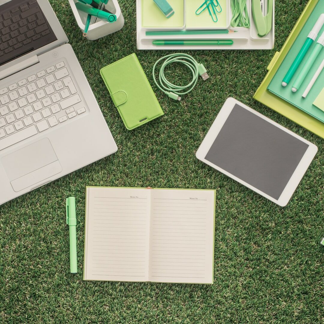 Business and sustainability Laptop and office supplies on the grass, blank organizer at center, green business concept